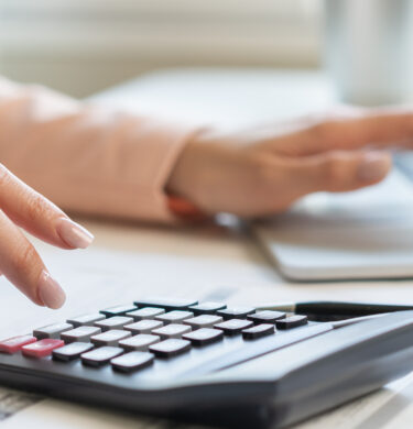 Main avec calculette et ordi sur un bureau