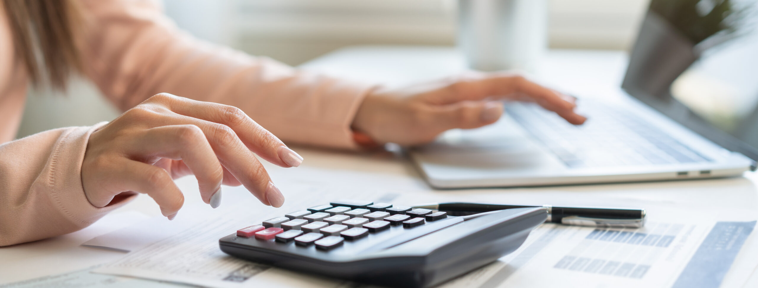Main avec calculette et ordi sur un bureau